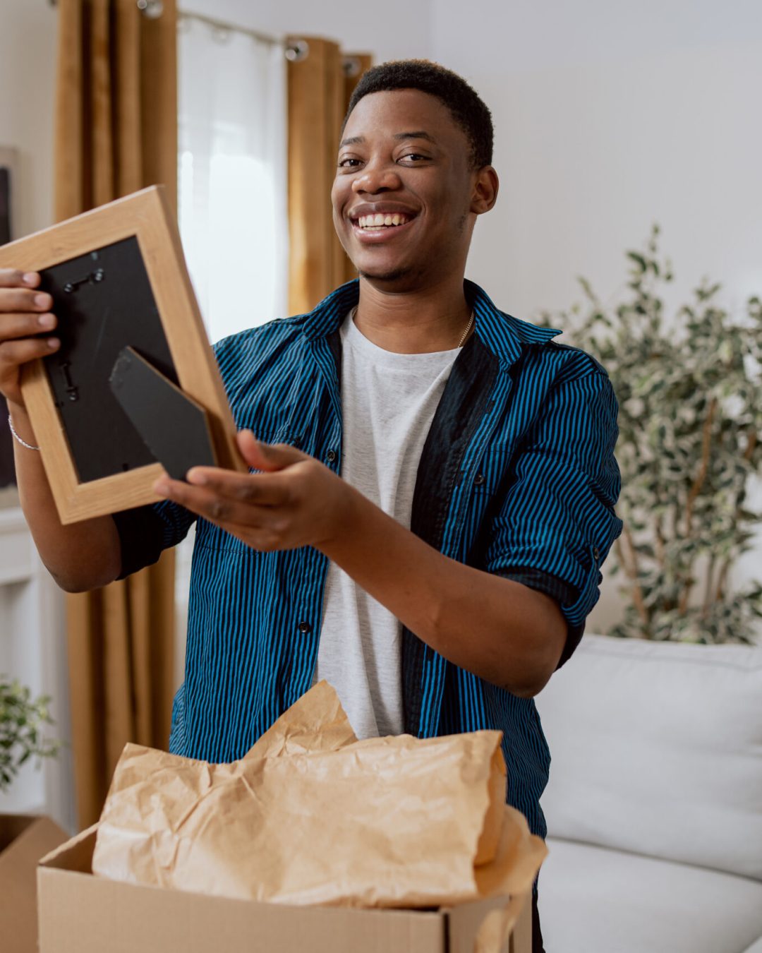 A men is cleaning in the living room after moving to a new apartment, unpacking cardboard boxes of things, the boy finds a picture in a frame from his childhood, he is shocked happy, watches with joy